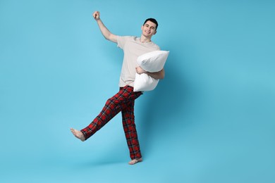 Happy man in pyjama holding pillow on light blue background