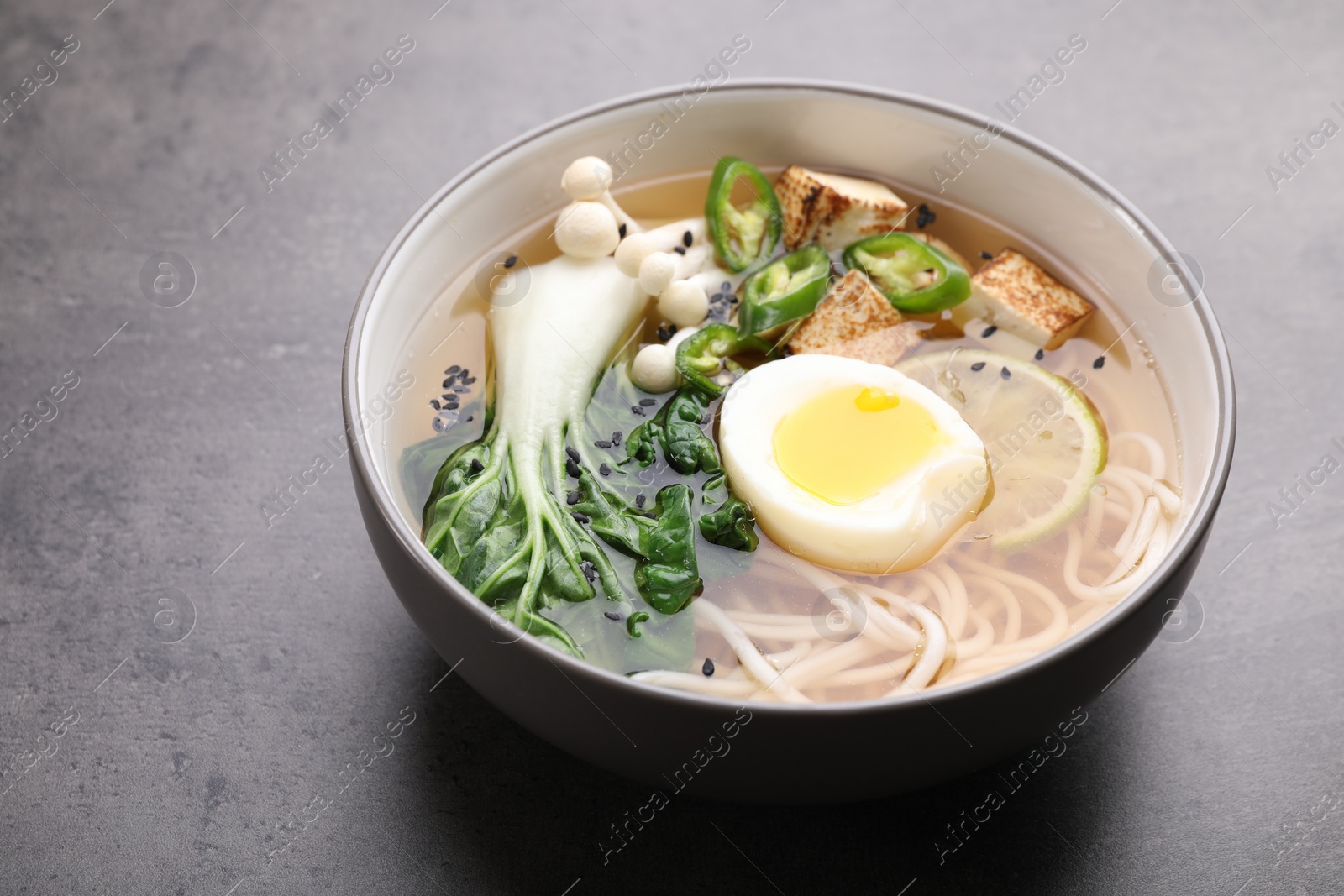 Photo of Bowl of vegetarian ramen on grey table, closeup