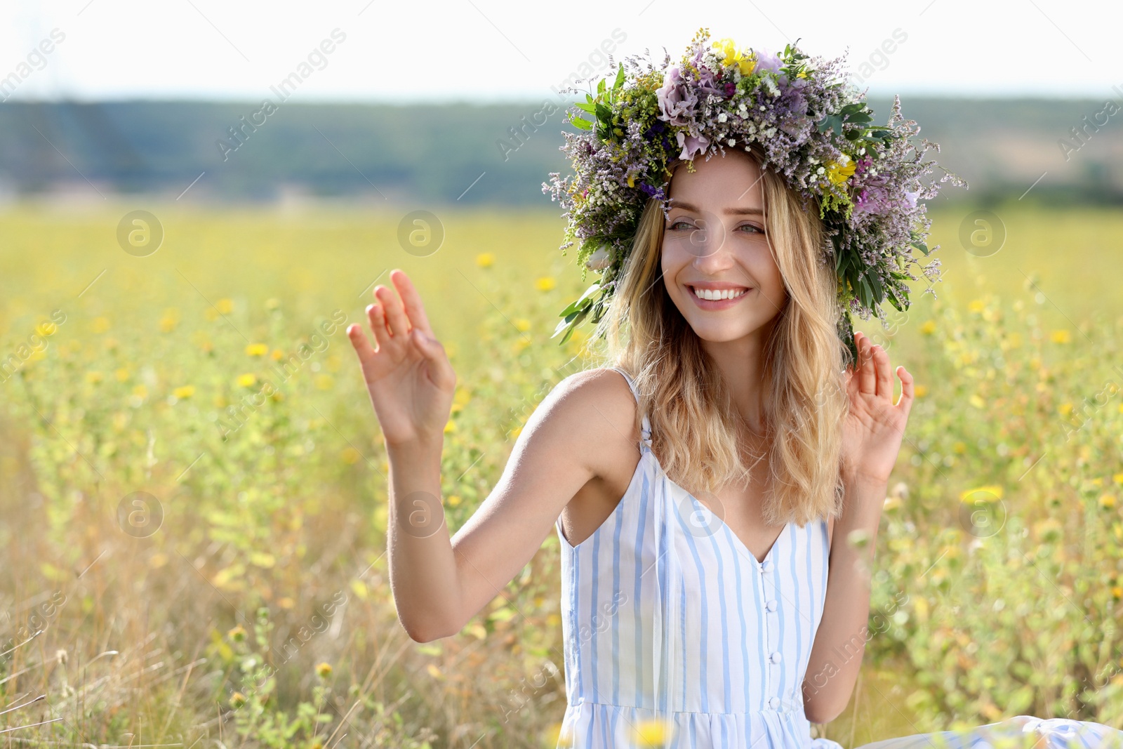 Photo of Young woman wearing wreath made of beautiful flowers in field on sunny day