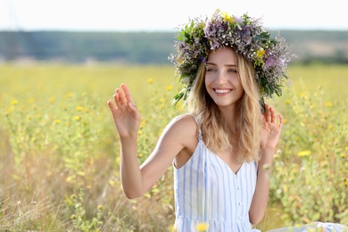 Photo of Young woman wearing wreath made of beautiful flowers in field on sunny day