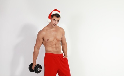 Sexy shirtless Santa Claus with dumbbell on light background, space for text