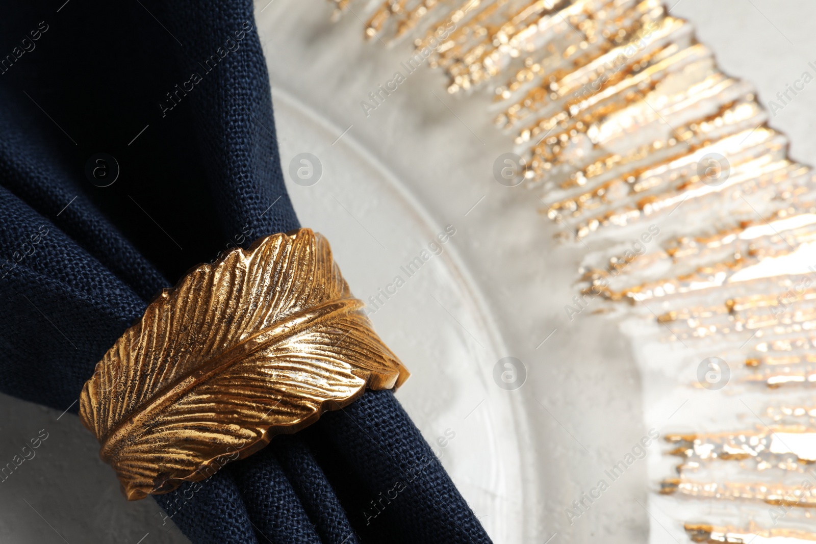 Photo of Dark blue fabric napkin and decorative ring for table setting on plate, closeup