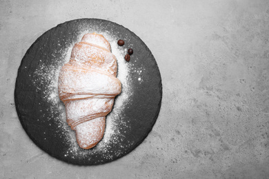 Photo of Tasty croissant with powdered sugar on grey table, space for text