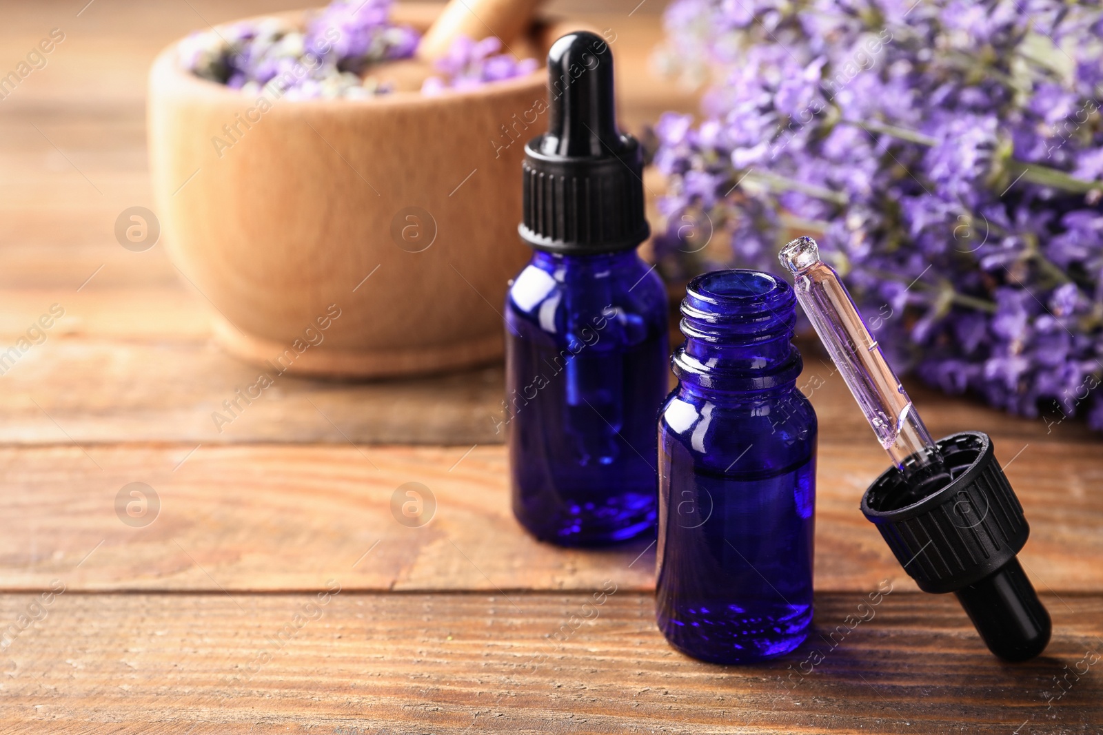 Photo of Bottles with natural lavender oil, dropper and flowers on wooden table, closeup view. Space for text