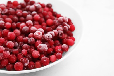 Photo of Frozen red cranberries in bowl on white table, closeup