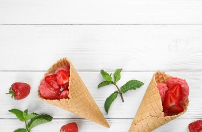 Photo of Delicious strawberry ice cream in wafer cones on white wooden table, flat lay. Space for text