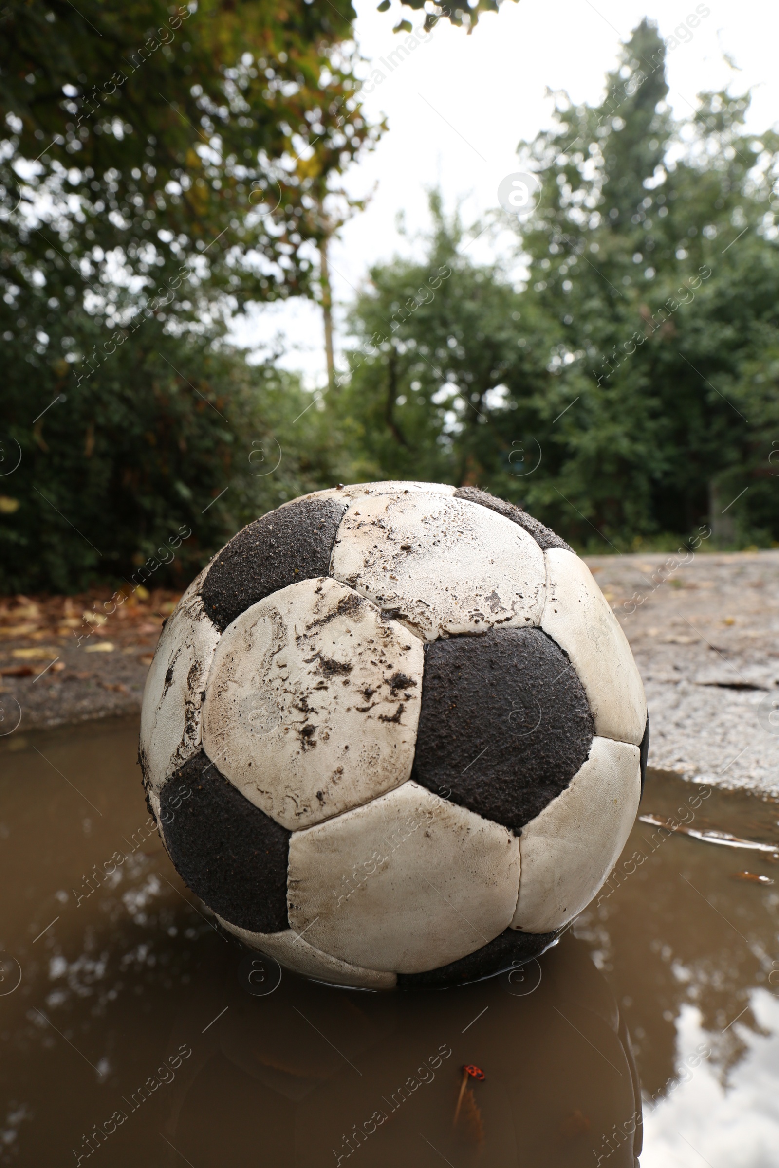 Photo of Dirty soccer ball in muddy puddle outdoors