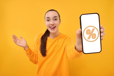 Image of Discount, offer, sale. Woman showing mobile phone with percent sign on screen, orange background