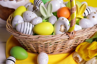 Photo of Wicker basket with festively decorated Easter eggs and beautiful tulips on white wooden table, closeup