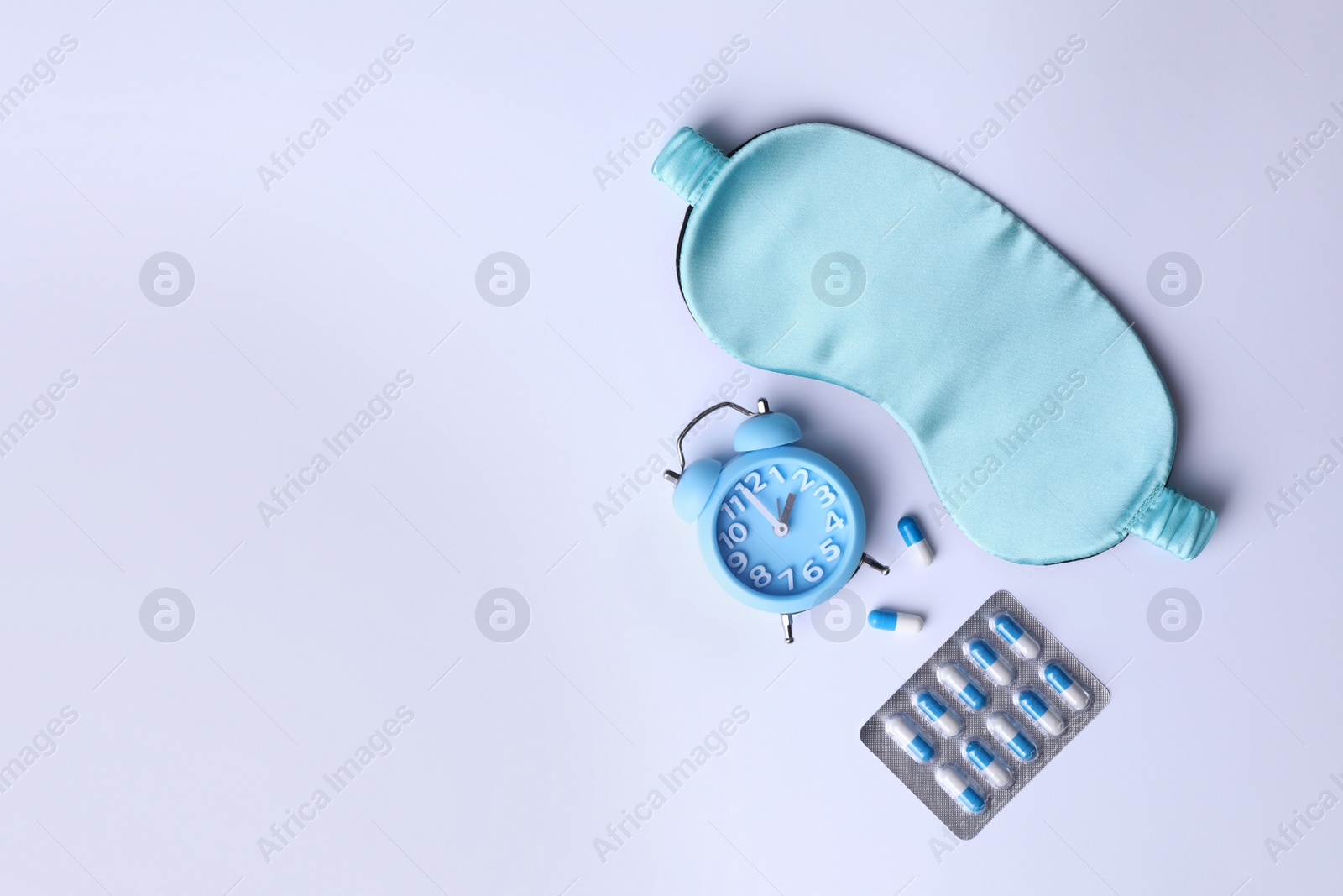 Photo of Sleeping mask, pills and alarm clock on white background, flat lay. Insomnia treatment