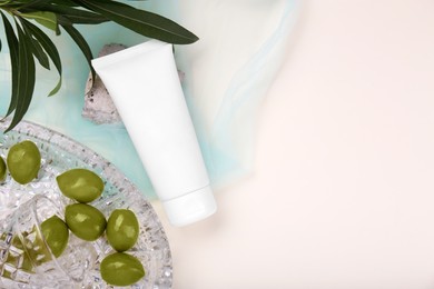 Photo of Tube of cream, olives, stone and leaves on beige background with light blue organza fabric drapery, flat lay. Space for text