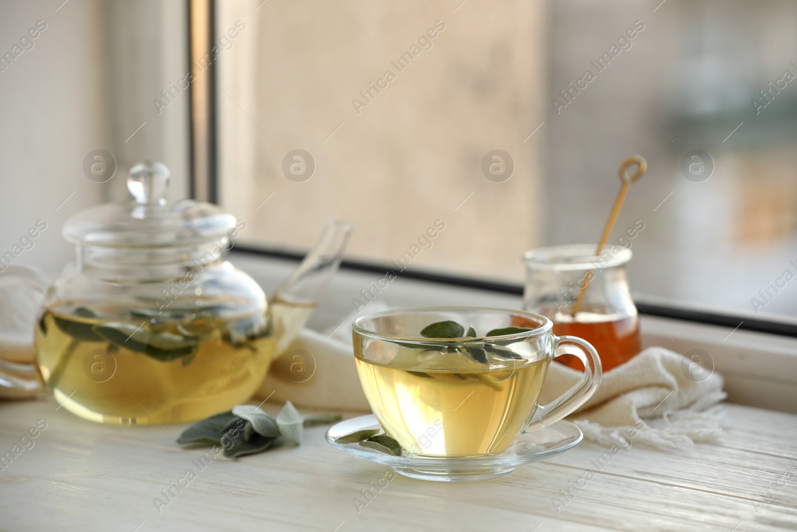 Photo of Sage tea and green leaves on white wooden windowsill