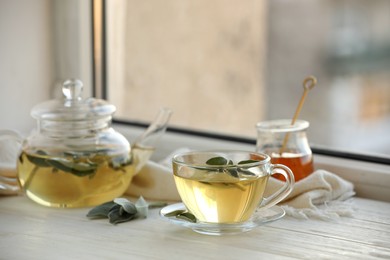 Photo of Sage tea and green leaves on white wooden windowsill