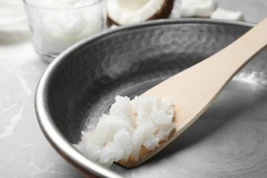 Frying pan with coconut oil and wooden spatula on grey marble table, closeup. Healthy cooking