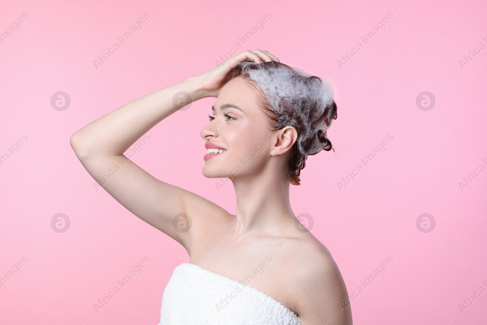 Photo of Happy young woman washing her hair with shampoo on pink background