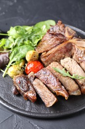 Photo of Delicious grilled beef meat, vegetables and greens on black table, closeup