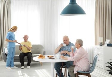 Photo of Nurse assisting elderly man while senior couple having breakfast at retirement home