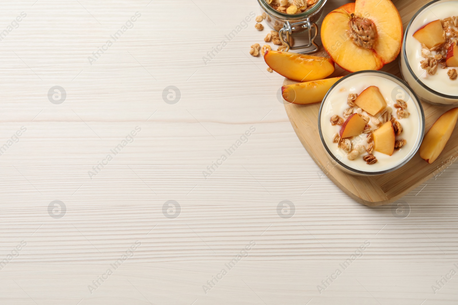 Photo of Delicious yogurt with fresh peach and granola on white wooden table, top view. Space for text