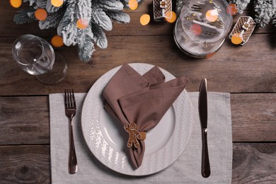 Plate with fabric napkin, cutlery and festive decor on wooden table, flat lay