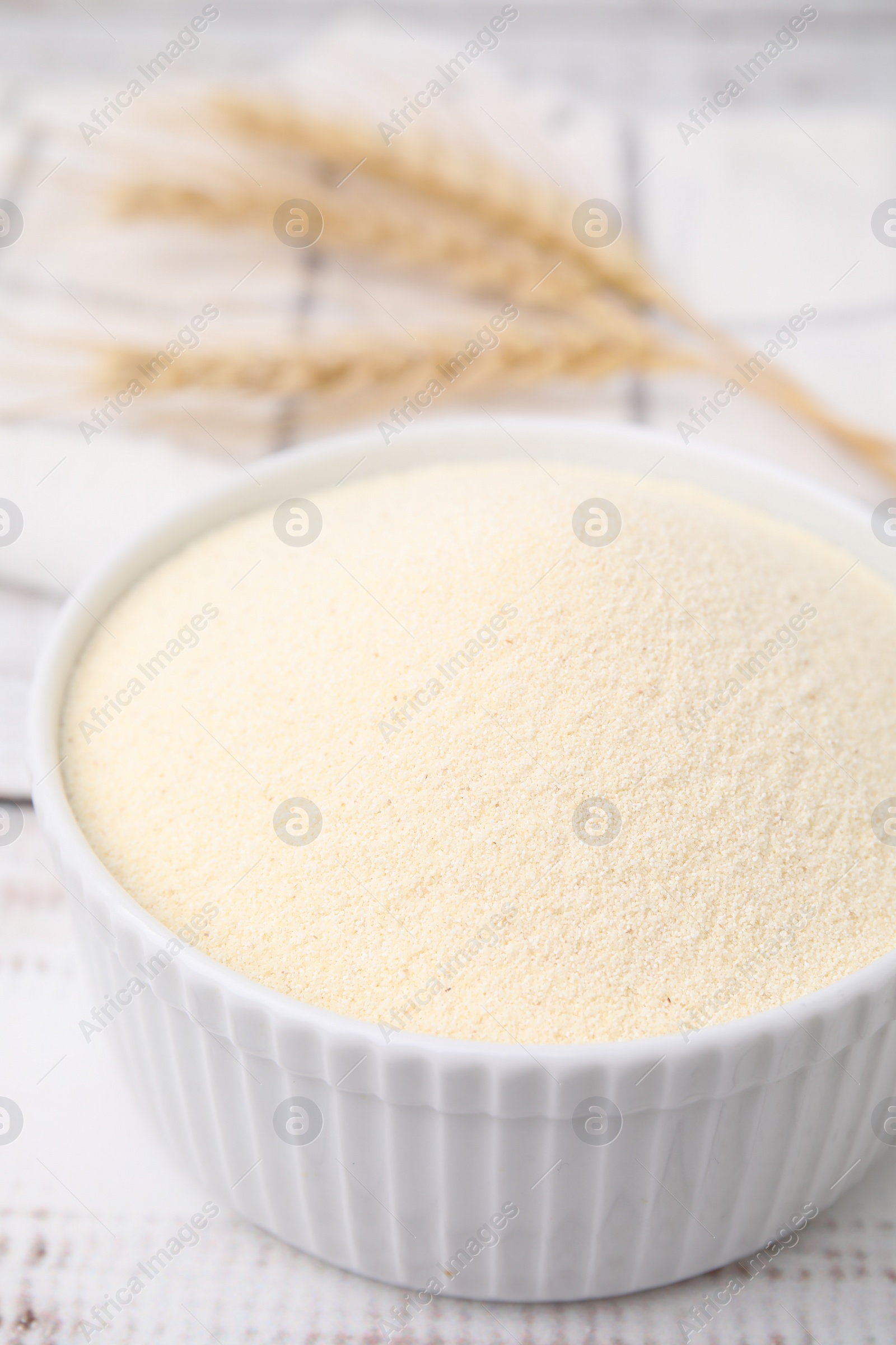 Photo of Uncooked organic semolina in bowl on white wooden table, closeup