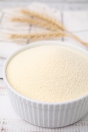 Photo of Uncooked organic semolina in bowl on white wooden table, closeup