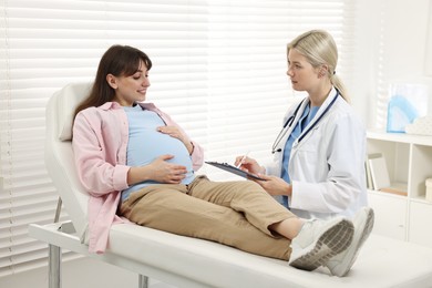 Photo of Doctor with clipboard consulting smiling pregnant patient in clinic