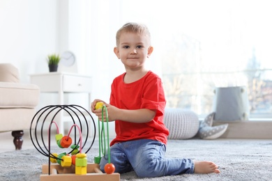 Photo of Cute child playing with bead maze on floor indoors