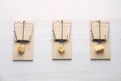Photo of Mousetraps with pieces of cheese on white wooden background, flat lay. Pest control