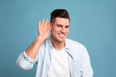 Photo of Man showing hand to ear gesture on light blue background