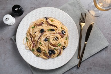 Delicious pasta with anchovies, olives and parmesan cheese served on grey table, flat lay