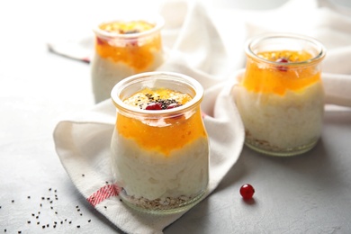 Photo of Creamy rice pudding with red currant, jam and oatmeal in jars on table
