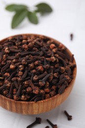 Photo of Aromatic cloves in bowl on white tiled table, closeup