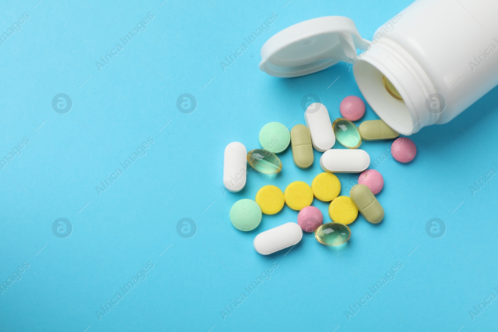 Photo of White bottle and different vitamin pills on light blue background, above view. Space for text