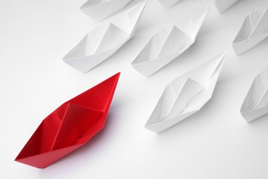 Paper boats following red one on white background, above view. Leadership concept