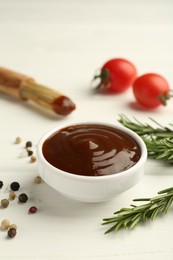 Photo of Tasty barbeque sauce in bowl, rosemary and spices on white wooden table