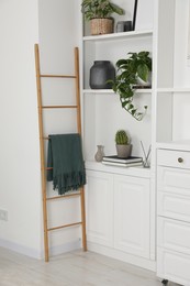 Wooden ladder near shelving unit with accessories and plants indoors