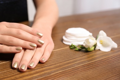 Photo of Woman with gold manicure at table, closeup. Nail polish trends