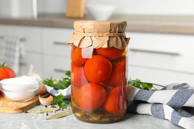 Jar with pickled tomatoes and vegetables on grey table in kitchen