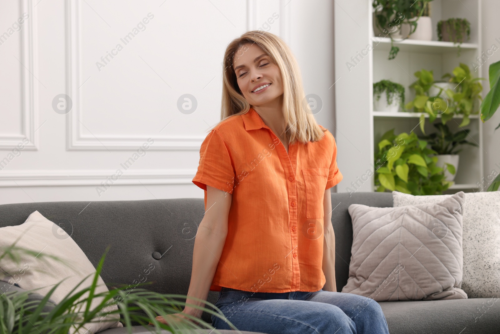 Photo of Woman sitting on sofa in room with beautiful houseplants