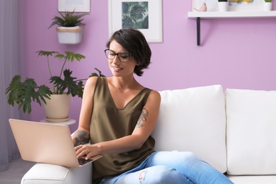 Young woman with modern laptop sitting on sofa at home