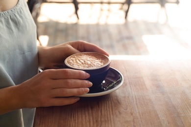 Photo of Woman with cup of fresh aromatic coffee at table, closeup