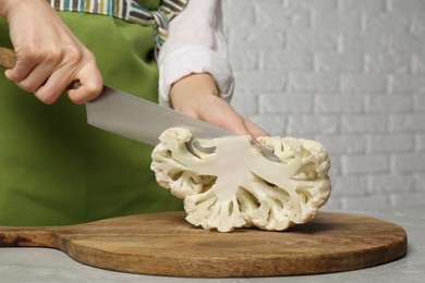 Photo of Woman cutting fresh cauliflower at light grey table, closeup