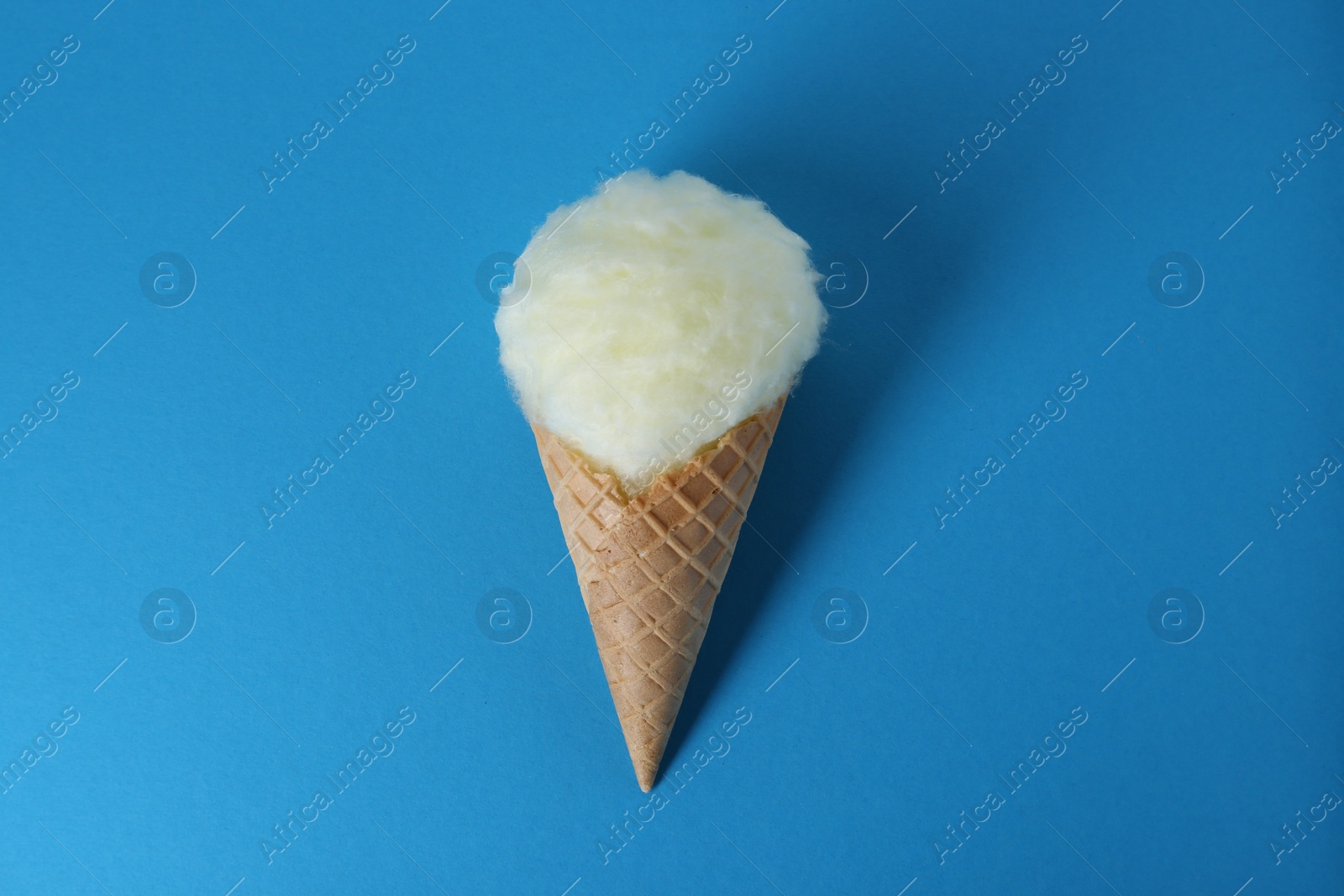 Photo of Sweet cotton candy in waffle cone on blue background, top view