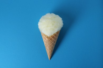 Photo of Sweet cotton candy in waffle cone on blue background, top view