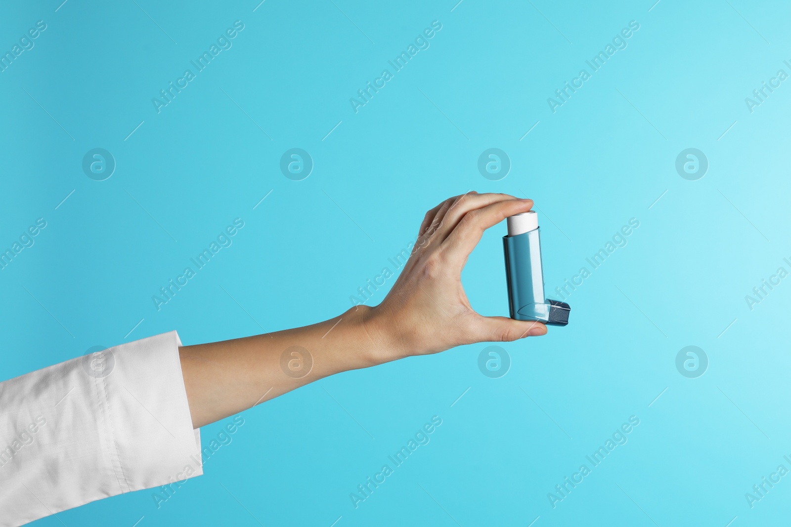 Photo of Female doctor holding asthma inhaler on color background, closeup. Medical object