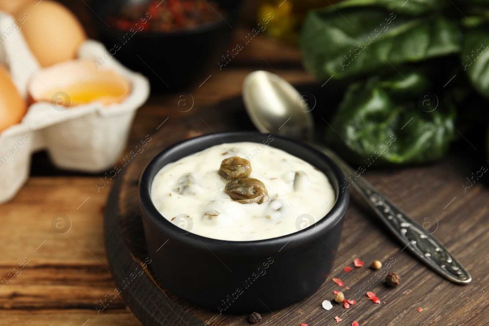 Photo of Caper sauce in bowl on wooden table, closeup