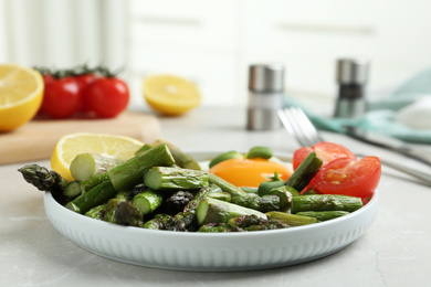 Oven baked asparagus served with fried egg on light grey marble table