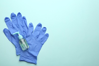 Photo of Medical gloves and hand sanitizer on light blue background, flat lay. Space for text