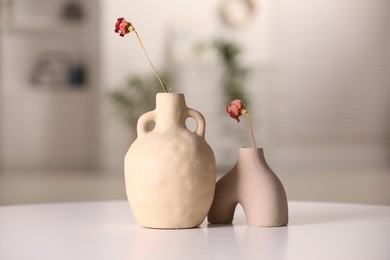 Vases with dried flowers on white table in room