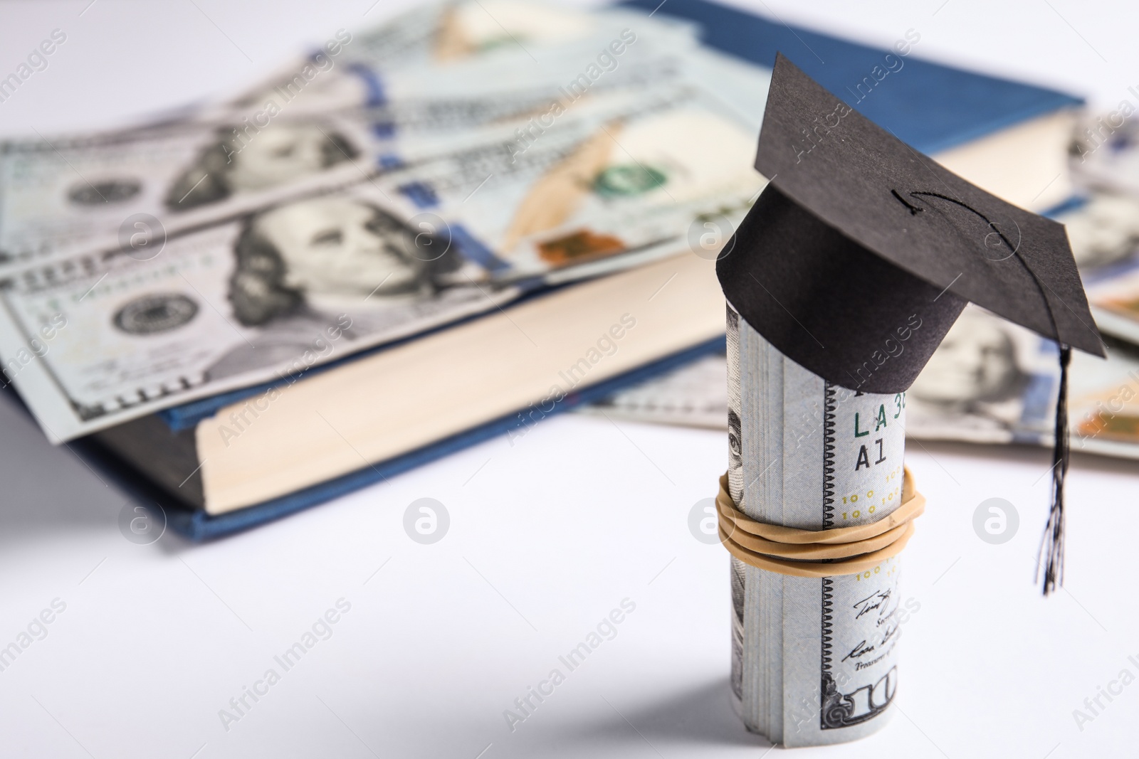 Photo of Dollar banknotes with mini student graduation hat and book on white background. Tuition fees concept